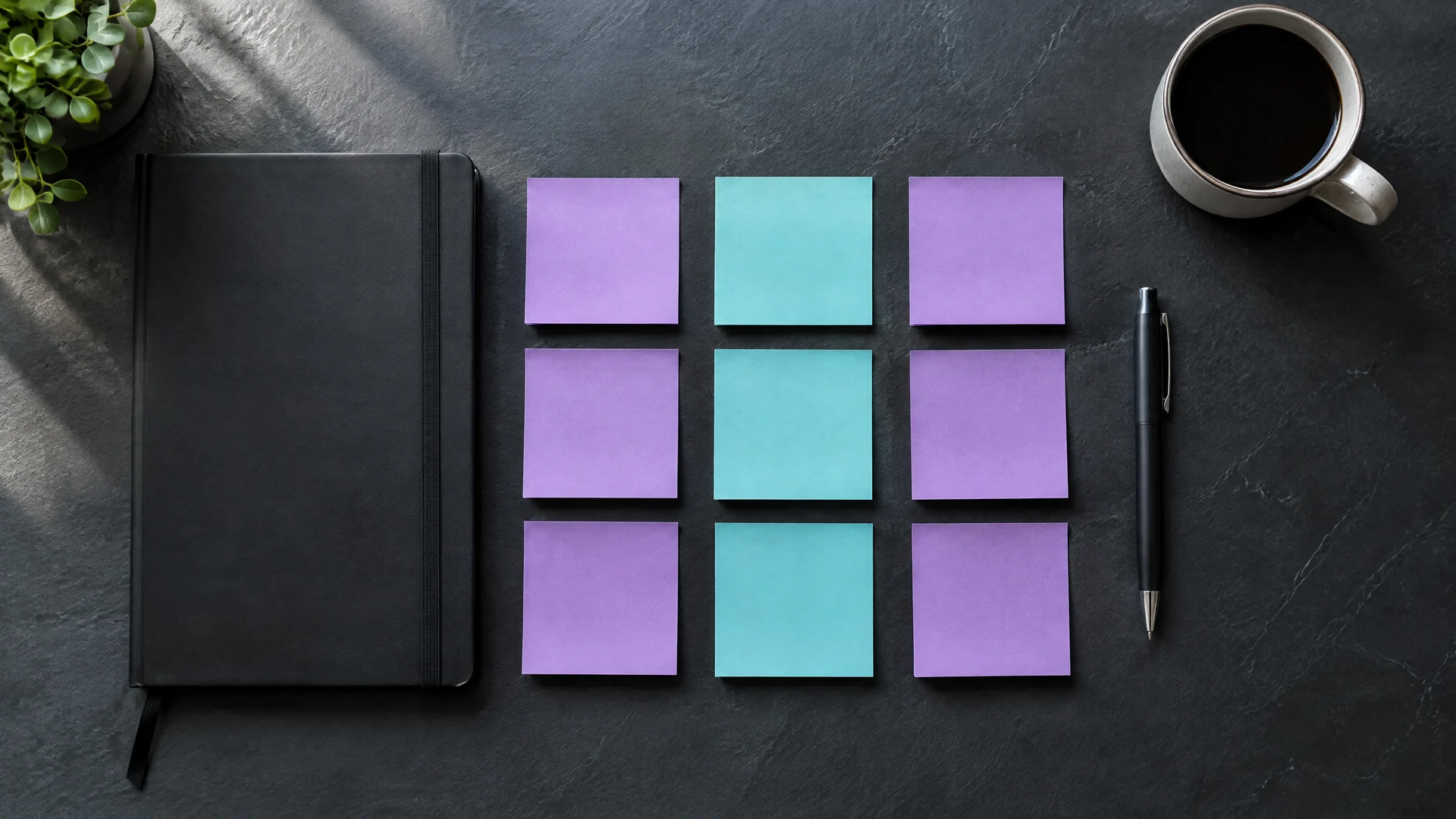 Blank violet and teal sticky notes in a grid beside a black notebook on a slate desk